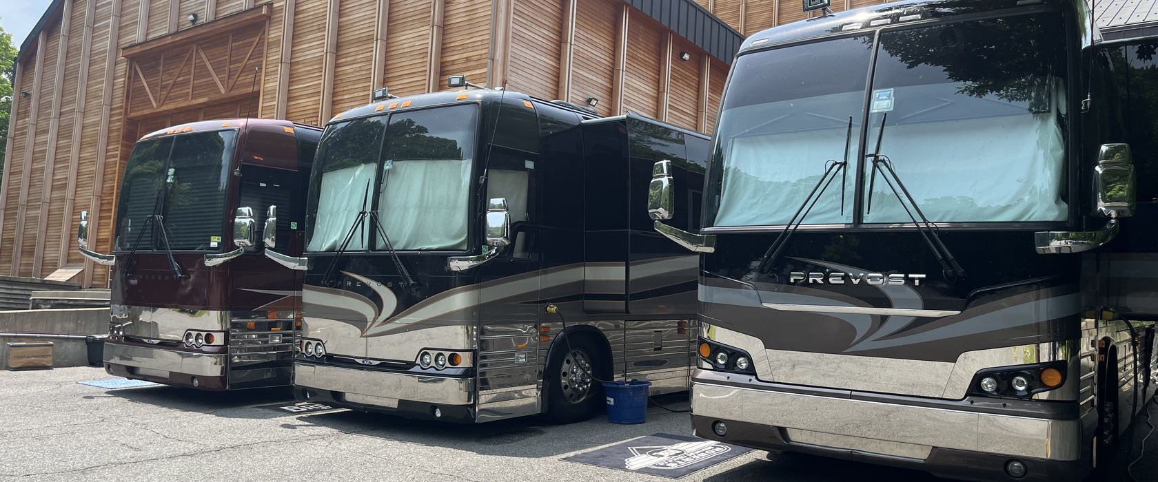 Three Prevost tour buses parked nose out at a wood clad venue.
