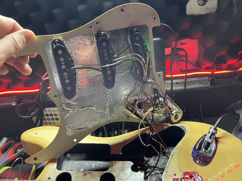 Scratch plate lifted off a Stratocaster, pickups and wiring exposed, the body open on the bench.