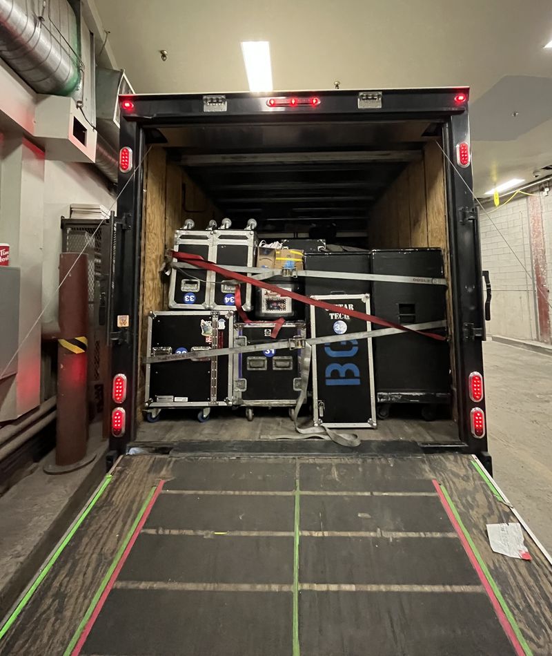 Back of a box truck at a loading dock, road cases strapped in and the ramp down.
