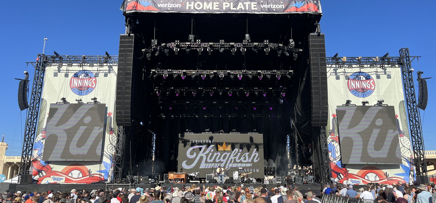Festival main stage in daylight, Christone Kingfish Ingram on the video wall, crowd at the barricade.