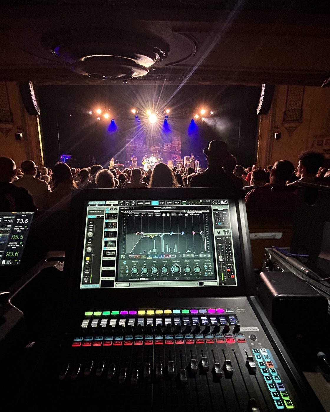 Front of house in a theatre, a Waves LV1 screen open on a dynamic EQ, band playing beyond the audience.