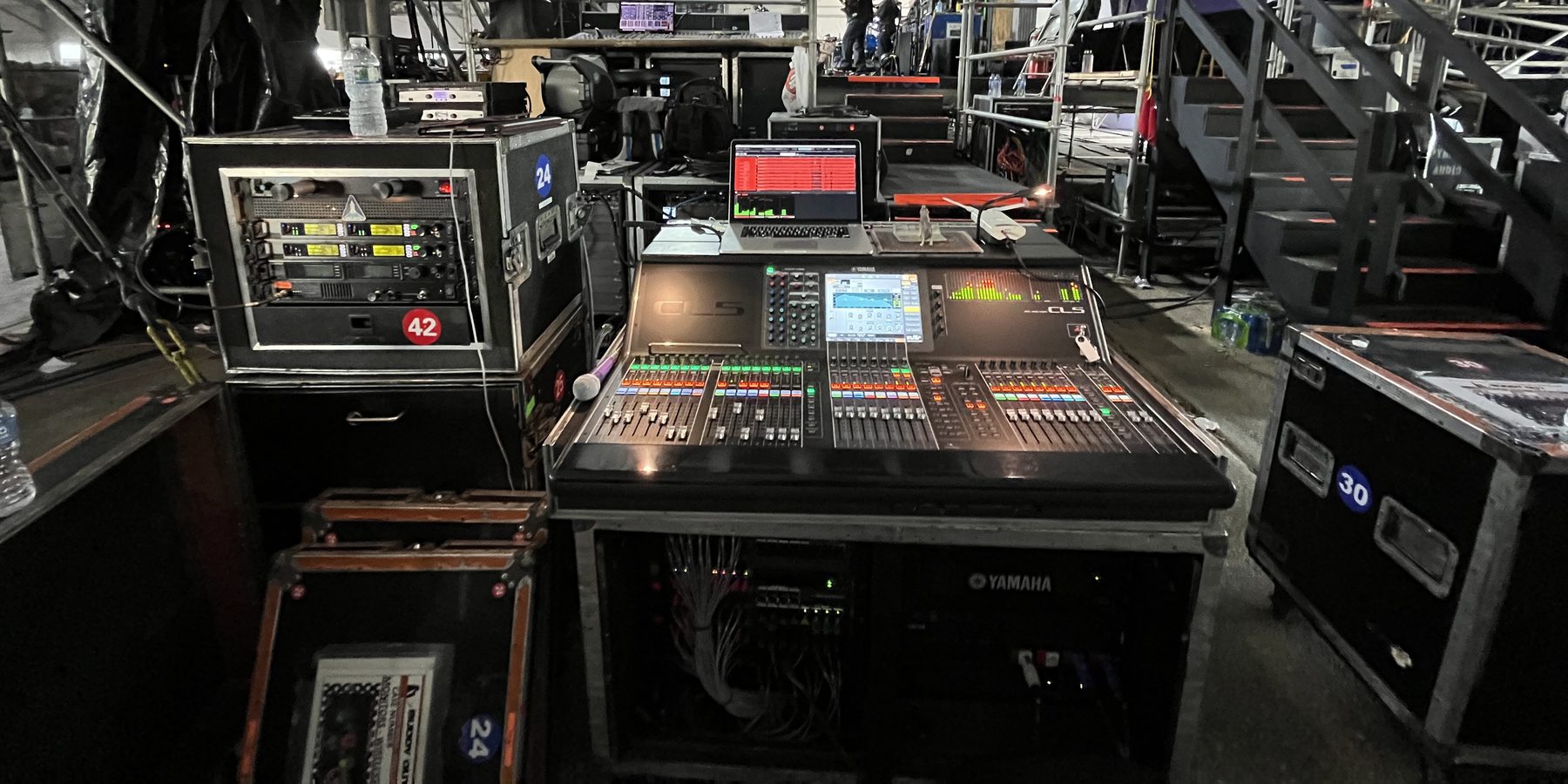 Yamaha CL5 at monitor world under the stage, laptop and a rack of wireless receivers beside it, road cases stacked around.